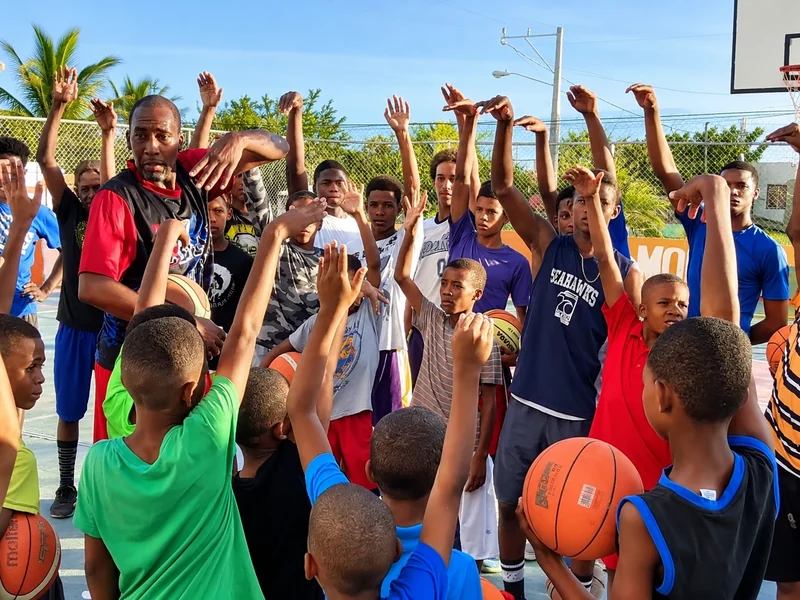 Cory McGee coaching a large group of young athletes with their hands raised at an N' Between Dreams basketball clinic